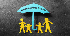 Image with paper cut outs of a family (two children and two adults) under an open umbrella. Umbrella has the words "Health Insurance Coverage" printed on it.