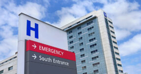 view of the outside of a hospital with a sign pointing to the Emergency entrance.