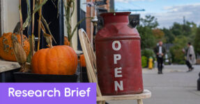 An open sign that is painted on an old can sitting on a chair on the sidewalk.